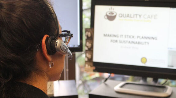 A person wearing a headset and looking at a computer screen.